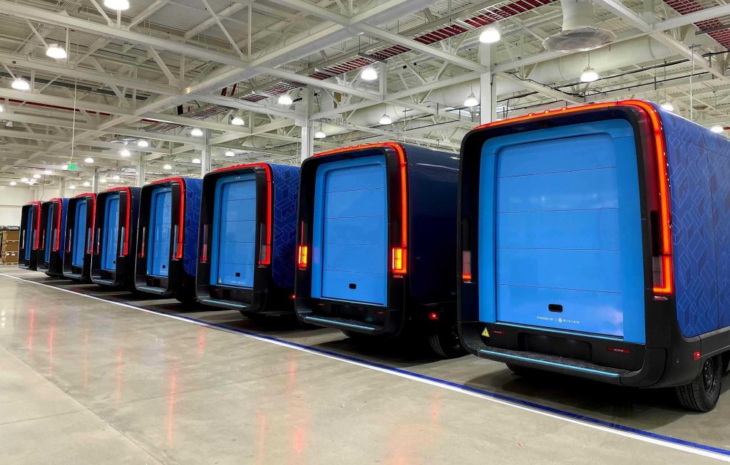 A row of commercial electric delivery vans staged inside a fleet depot